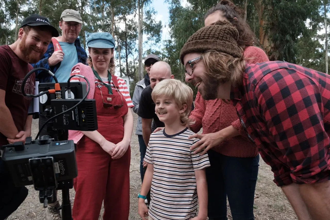 A crew member in a beanie showing a family and crew the shot on a camera monitor outdoors