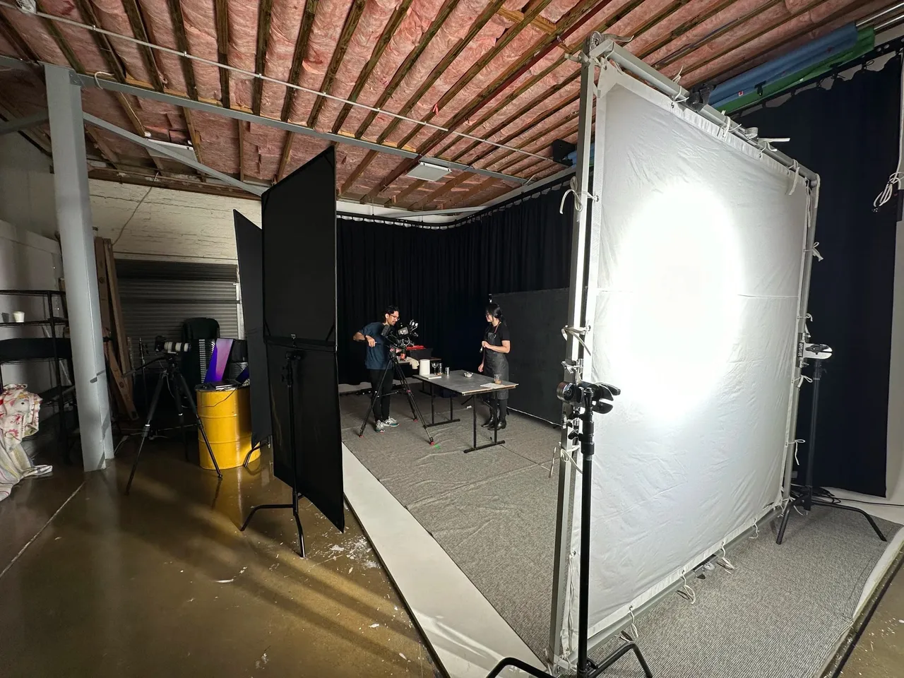 A large studio lighting setup with a diffusion frame under a timber and brick ceiling